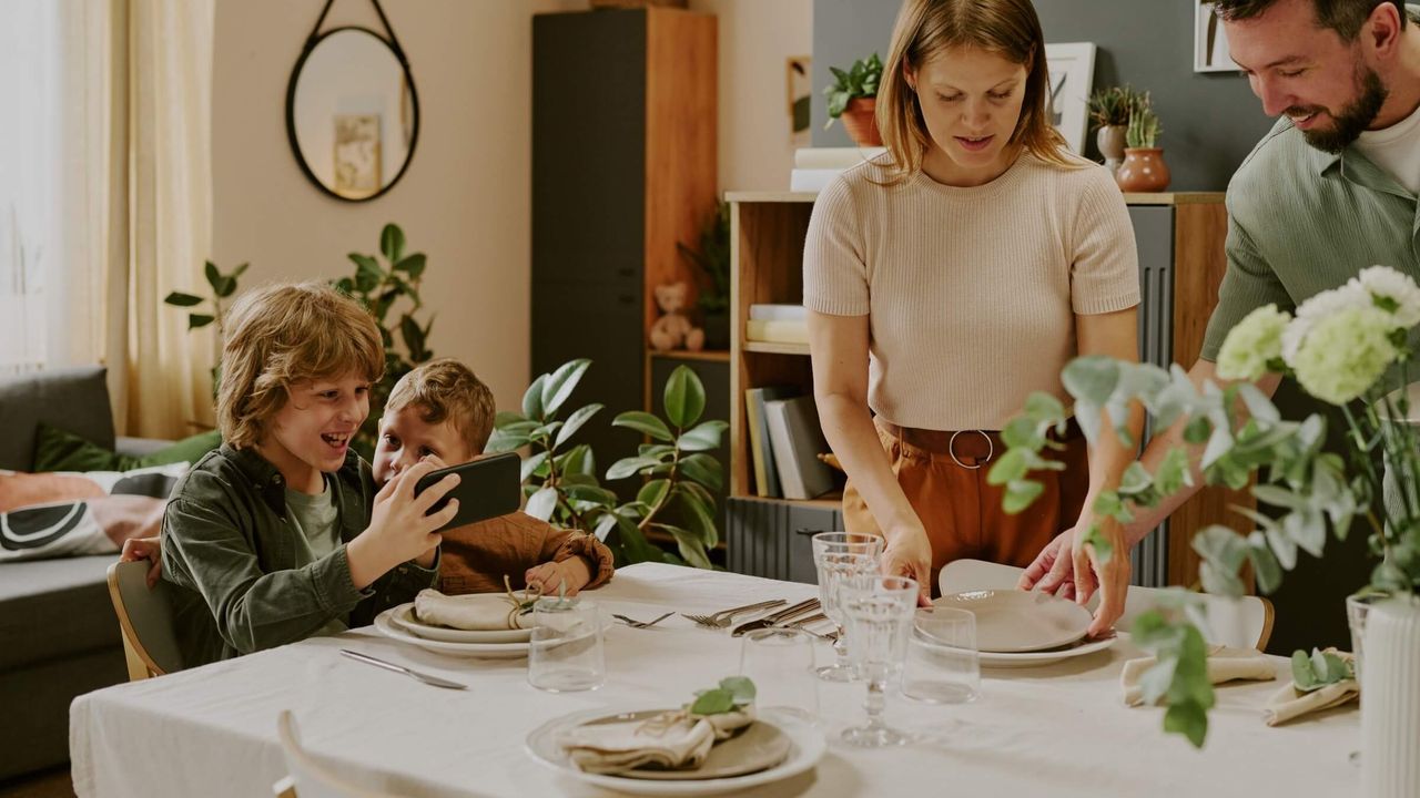 Brüder machen ein Handyfoto, während die Familie den Tisch deckt