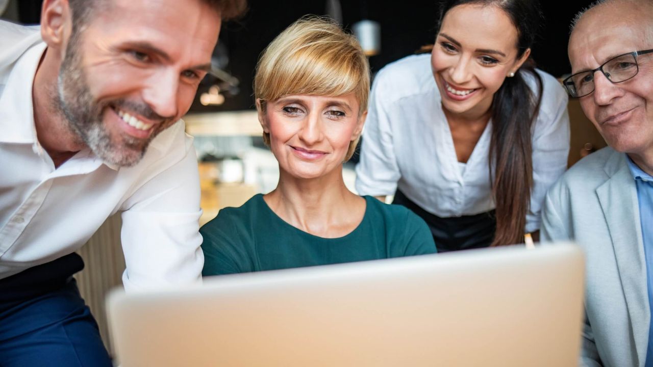 Businessleute schauen in einem Café auf einen Laptop und diskutieren gemeinsam