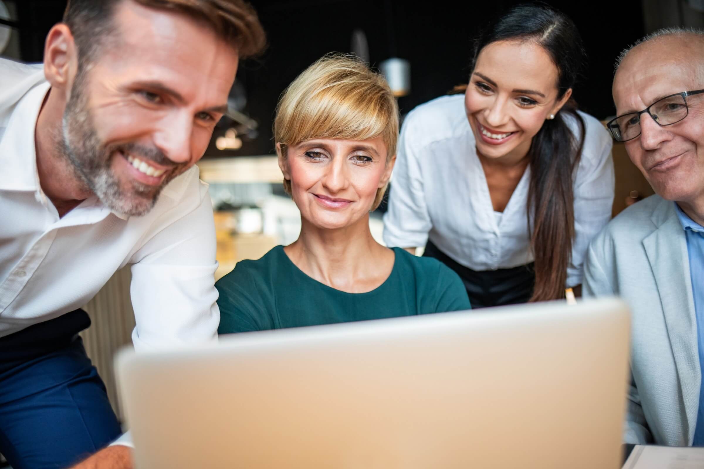 Businessleute schauen in einem Café auf einen Laptop und diskutieren gemeinsam