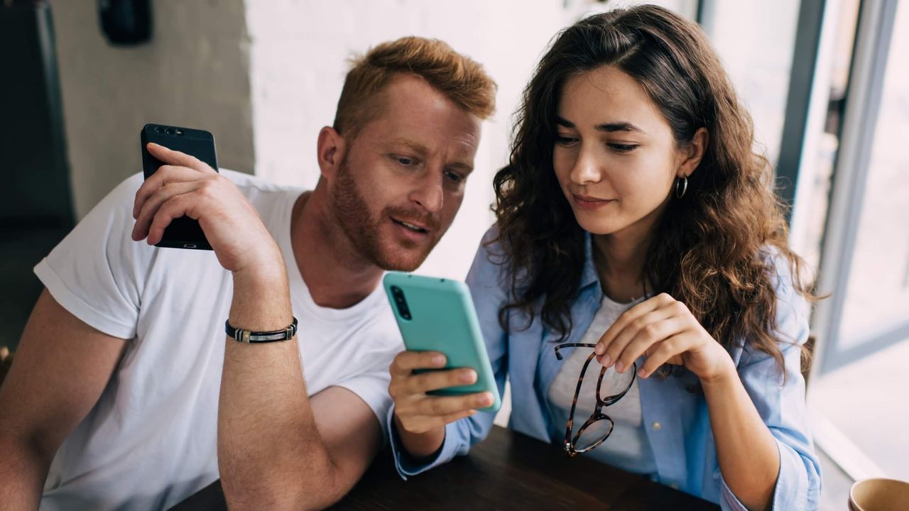Paar nutzt ein Smartphone und unterhält sich in einem modernen Café