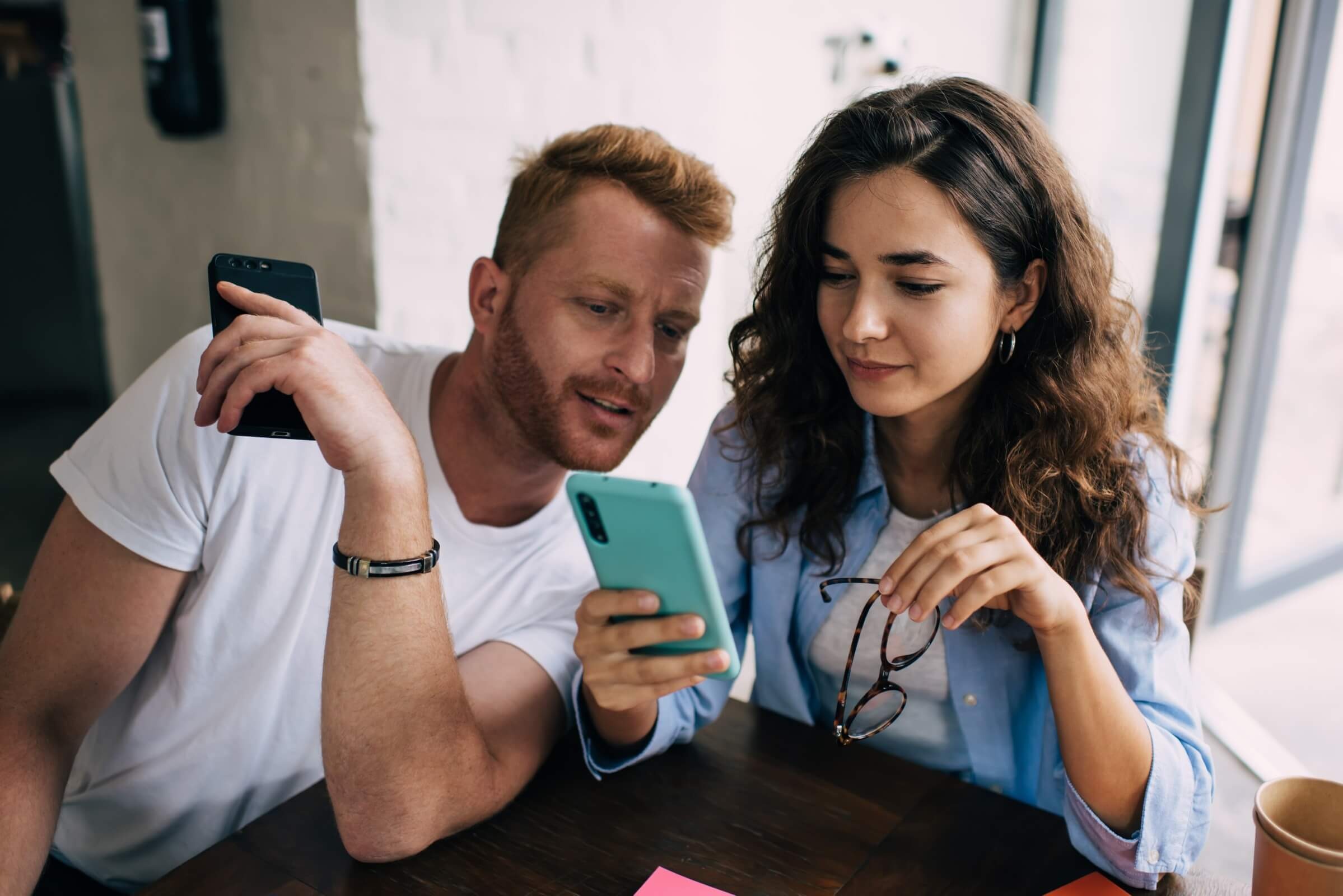Paar nutzt ein Smartphone und unterhält sich in einem modernen Café