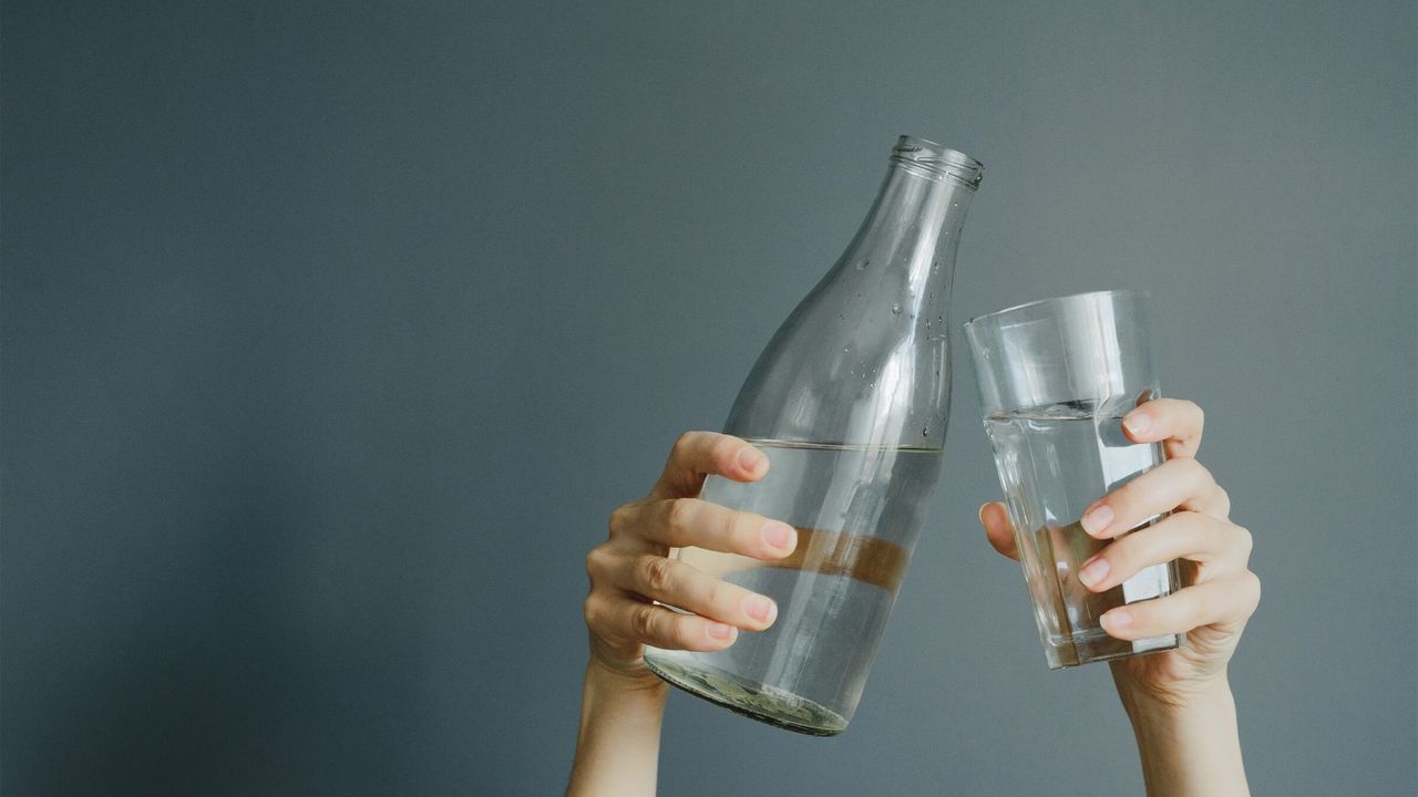 Hände halten ein Glas und eine Wasserflasche