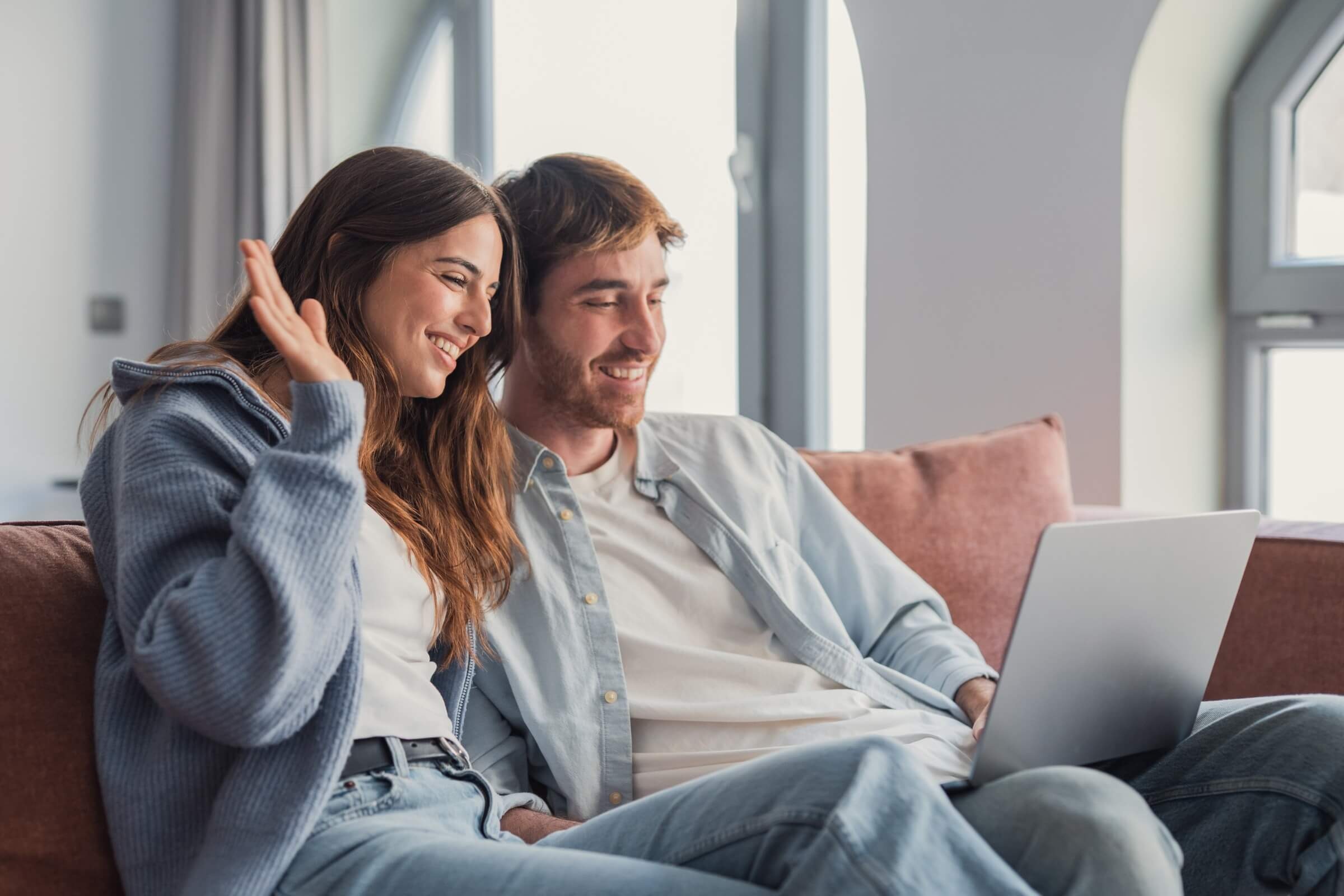Glückliches junges Paar winkt während eines Videoanrufs am Laptop.