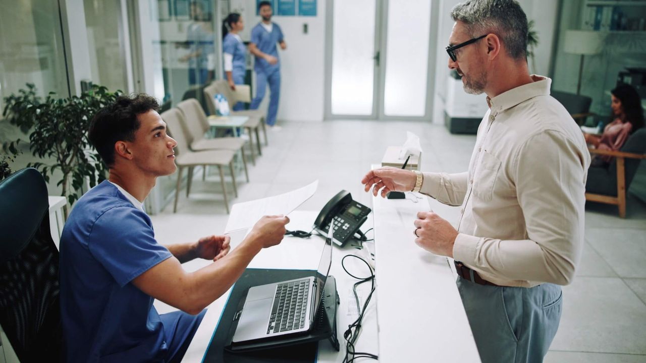 Krankenpflegerin und älterer Mann mit Unterlagen in der Krankenhauslobby