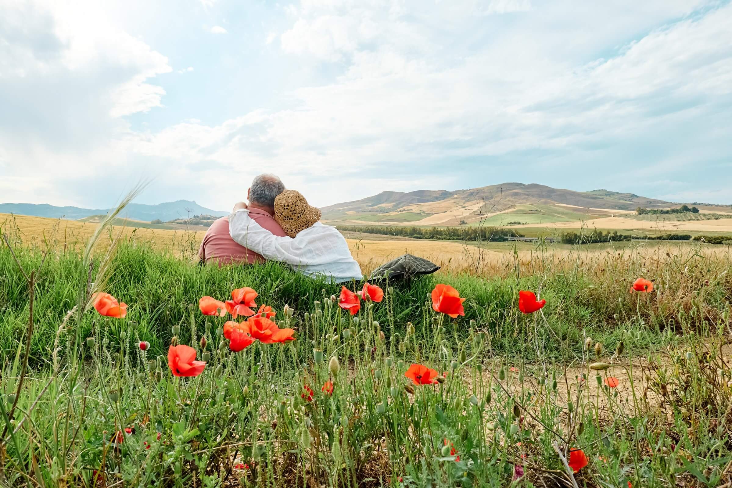 Mittelaltes Paar sitzt umarmt in einer Mohnblumenwiese