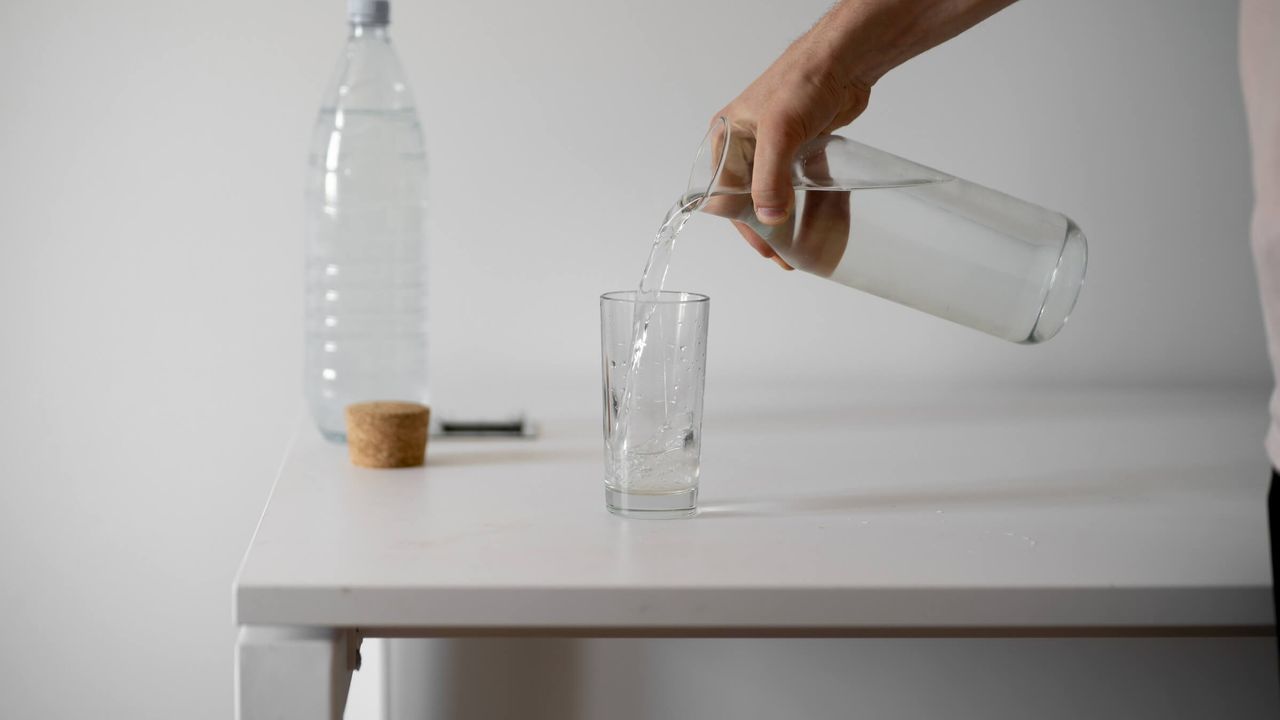 Person gießt erfrischendes Wasser in ein Glas in Innenräumen