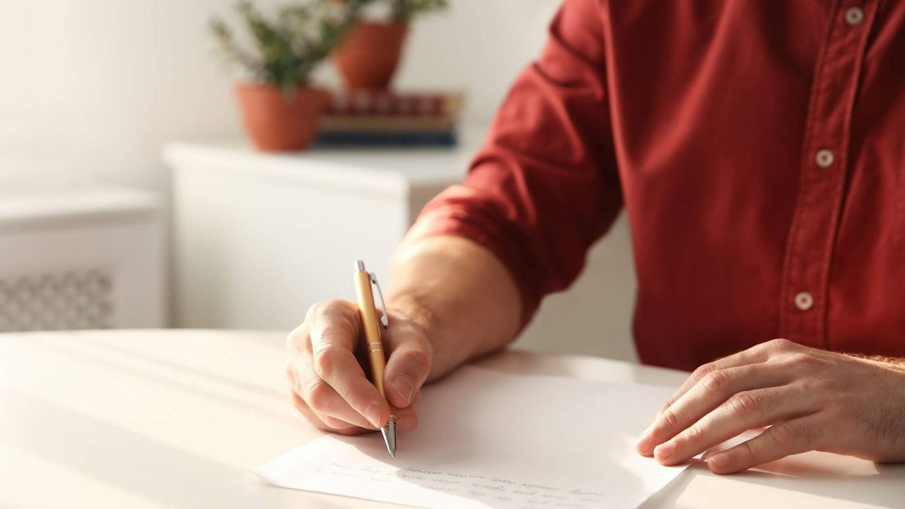 Person schreibt an einem Tisch in Innenräumen auf Papier