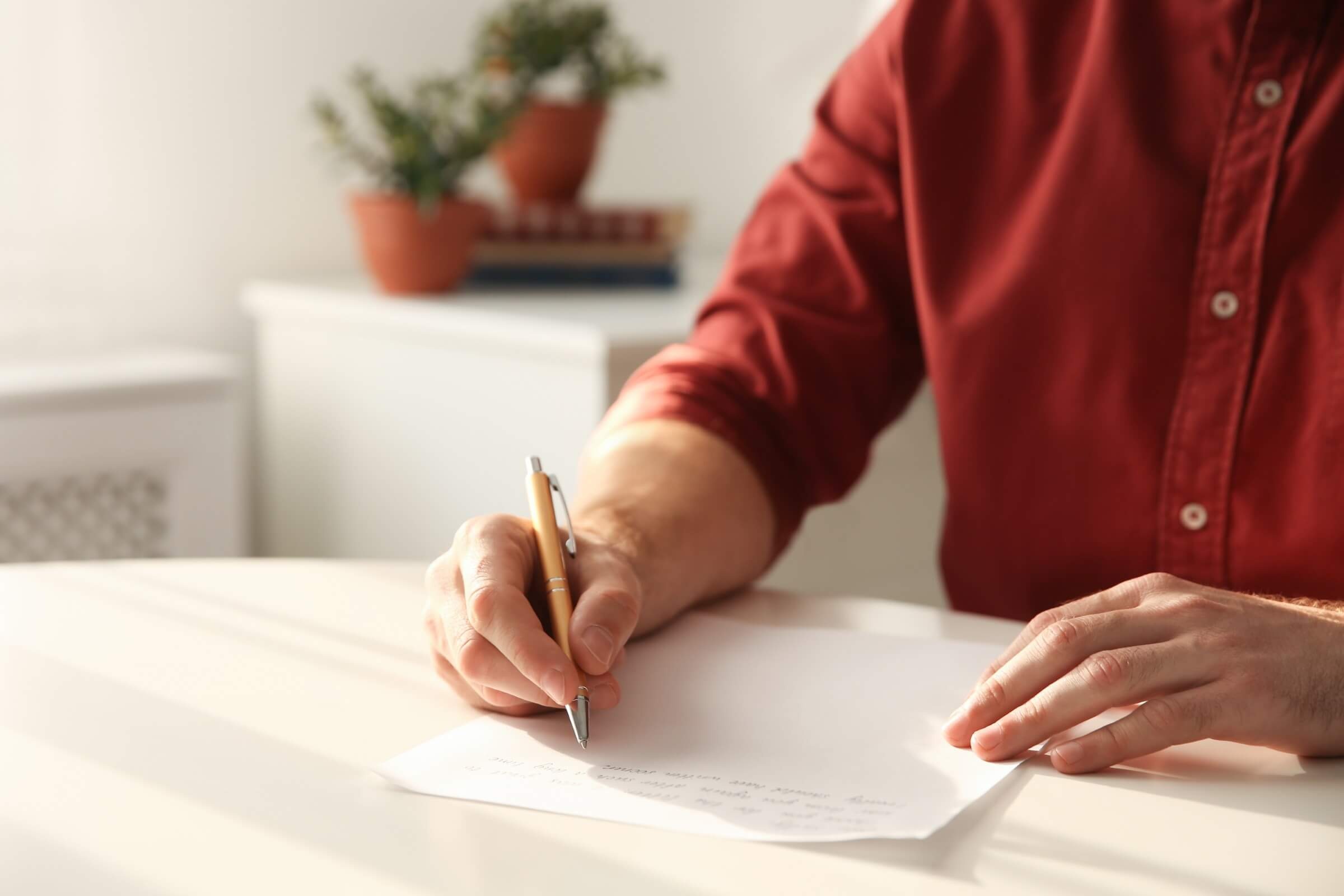 Person schreibt an einem Tisch in Innenräumen auf Papier