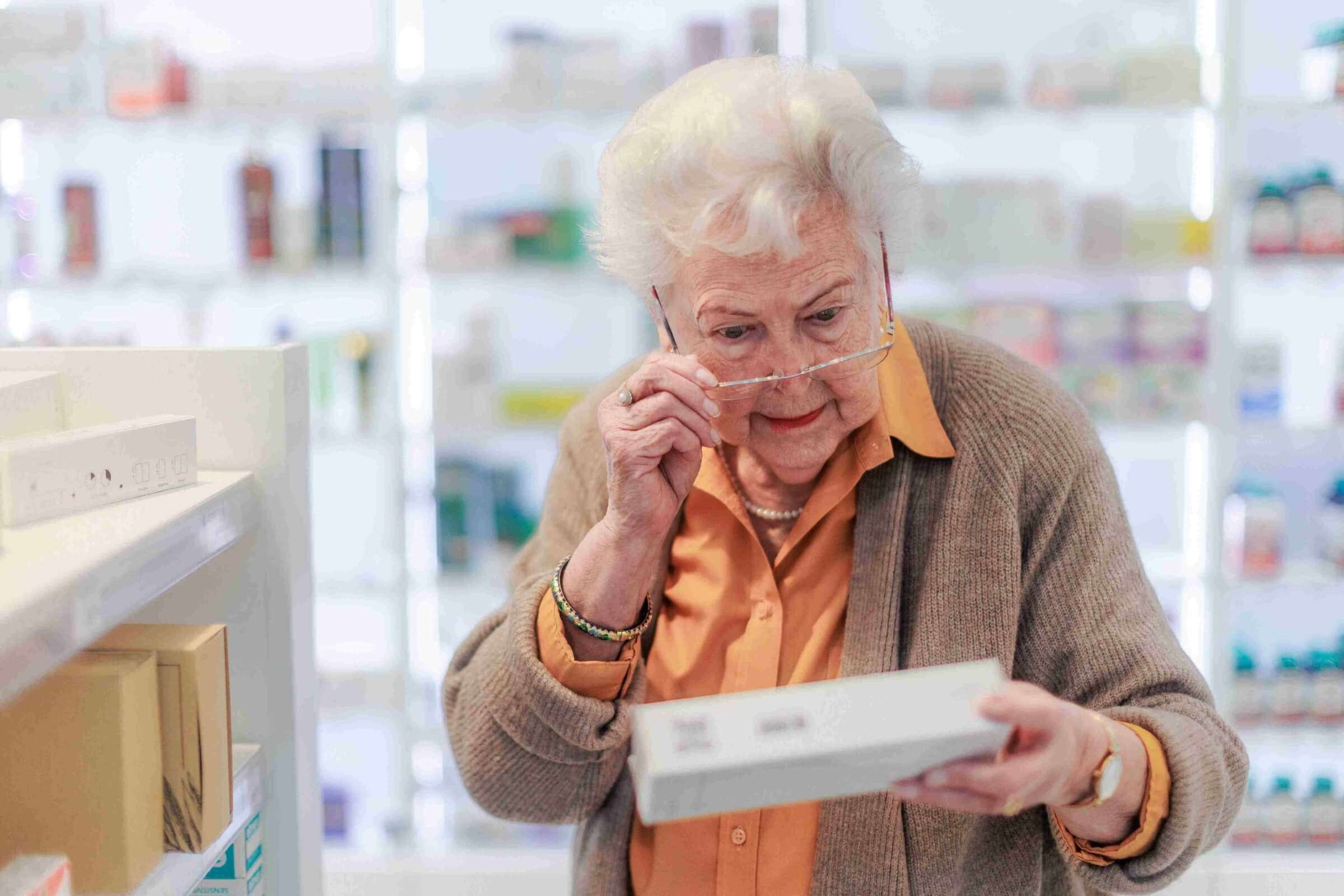 Seniorin liest ein Etikett im Apothekengang