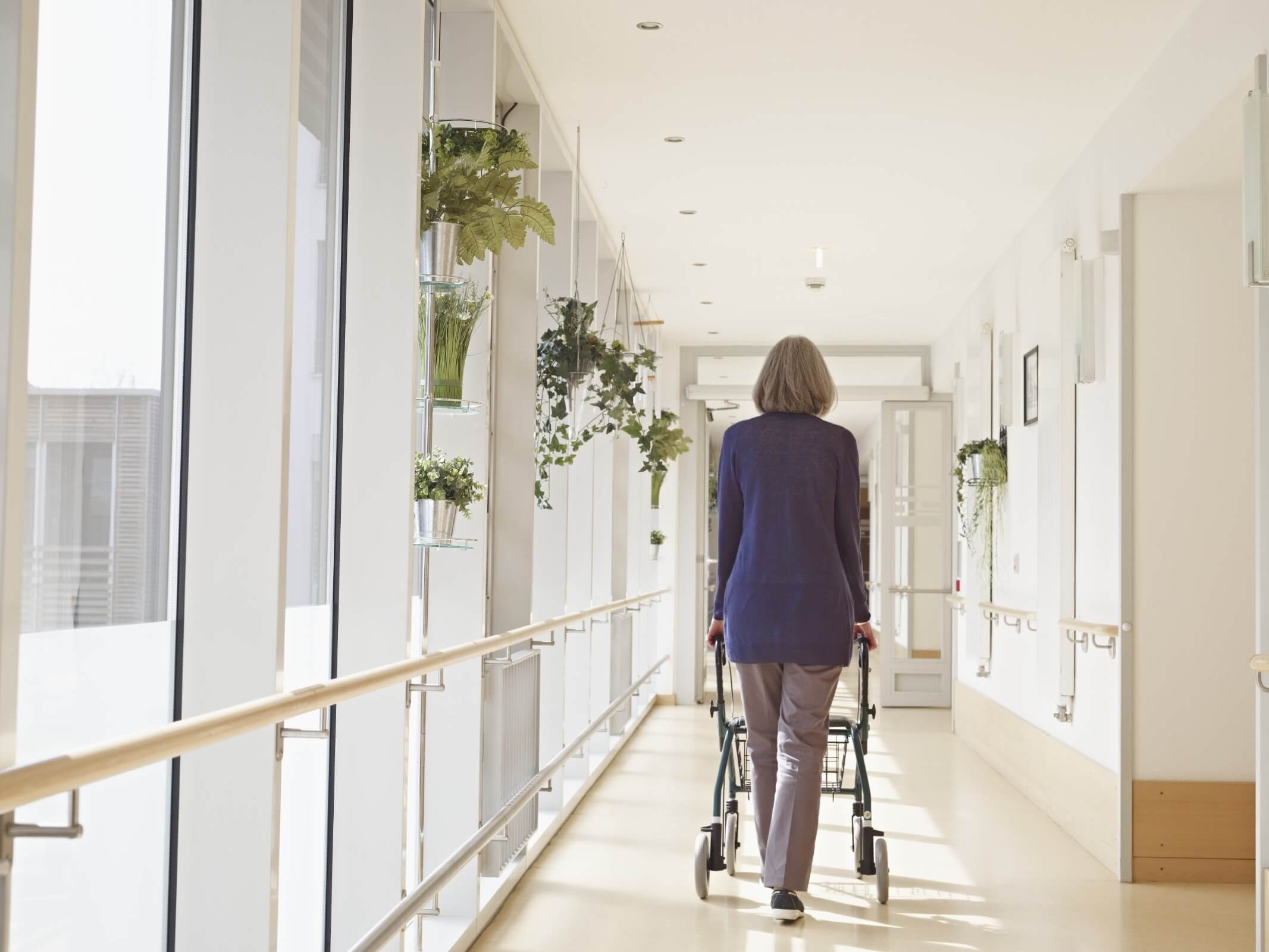 Seniorin läuft mit einer Gehhilfe durch den Gang im Spital
