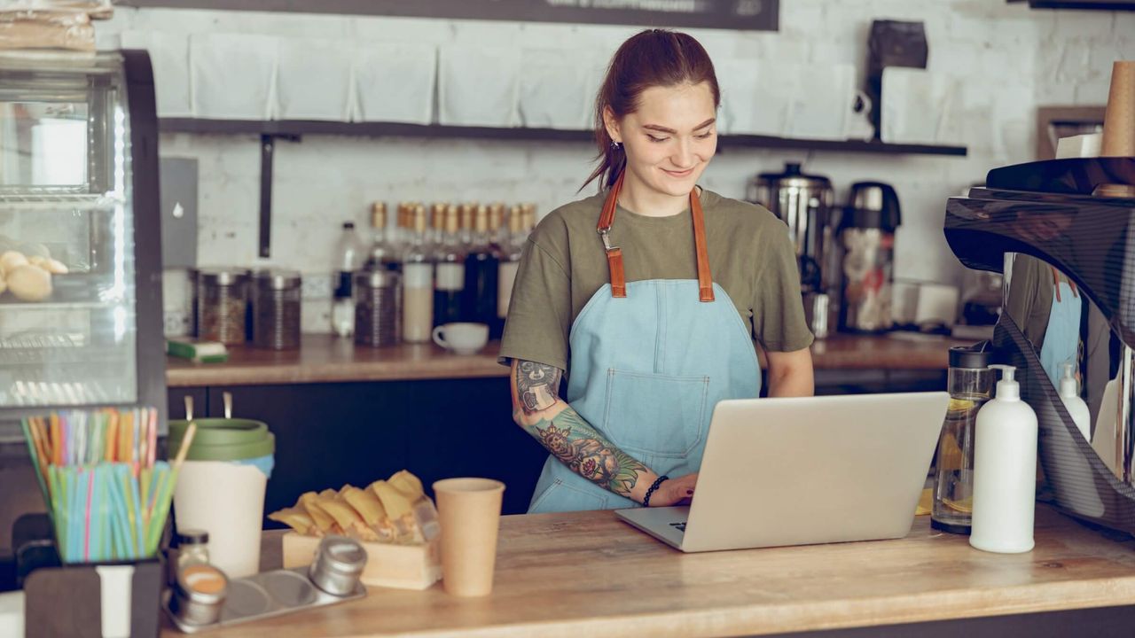 Lächelnde Barista arbeitet mit einem Notebook im Café