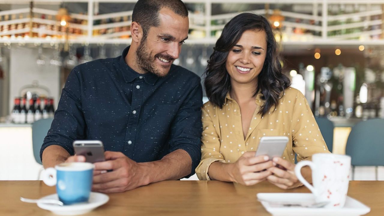 Lächelnder Mann und Frau genießen eine Kaffeepause und nutzen ihre Smartphones