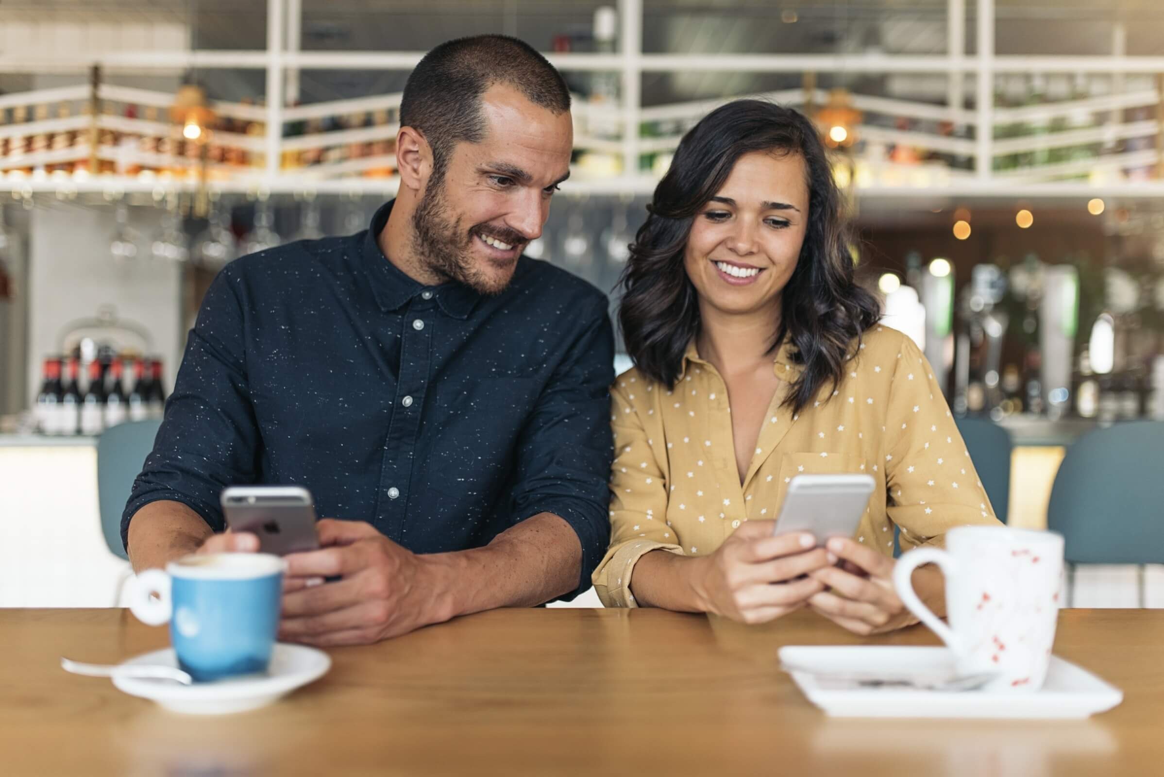 Lächelnder Mann und Frau genießen eine Kaffeepause und nutzen ihre Smartphones