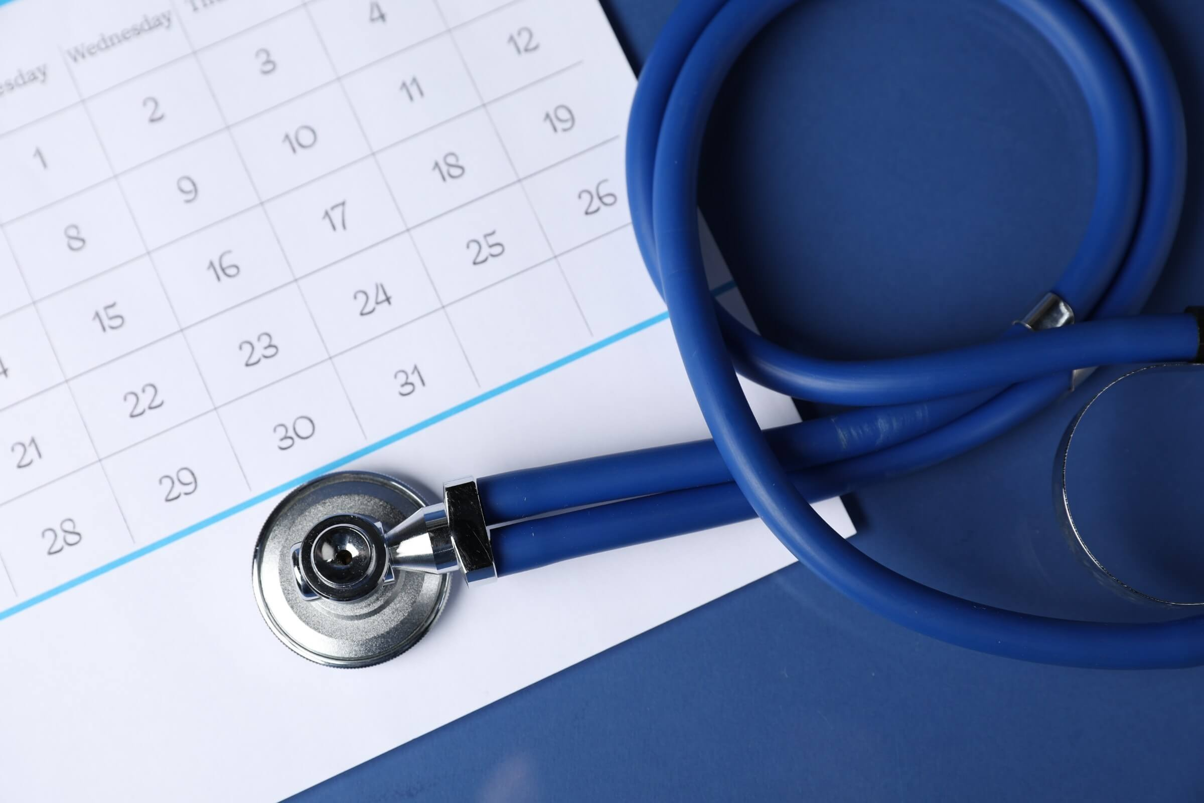 Stethoskop und Kalender auf blauem Hintergrund, Ansicht von oben