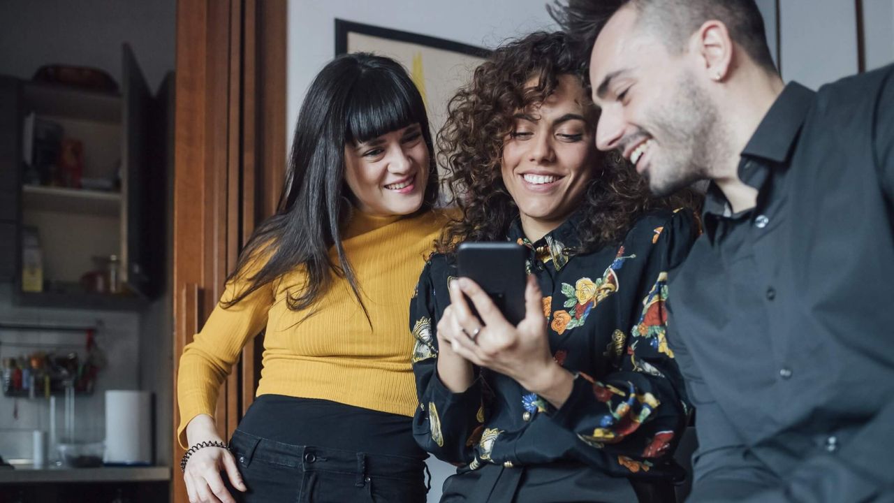 Drei Freunde lachen, während sie gemeinsam auf ein Handy schauen