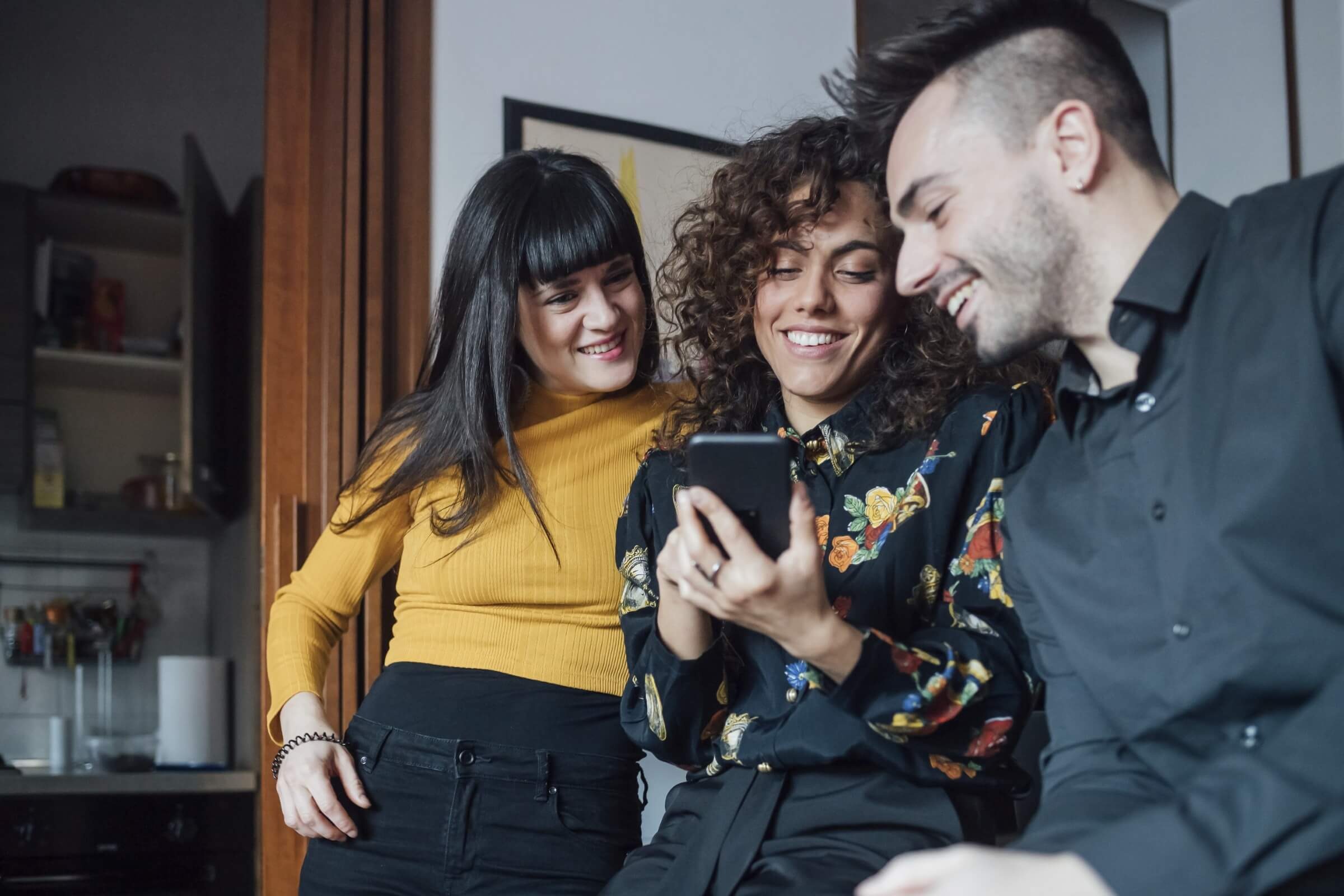 Drei Freunde lachen, während sie gemeinsam auf ein Handy schauen