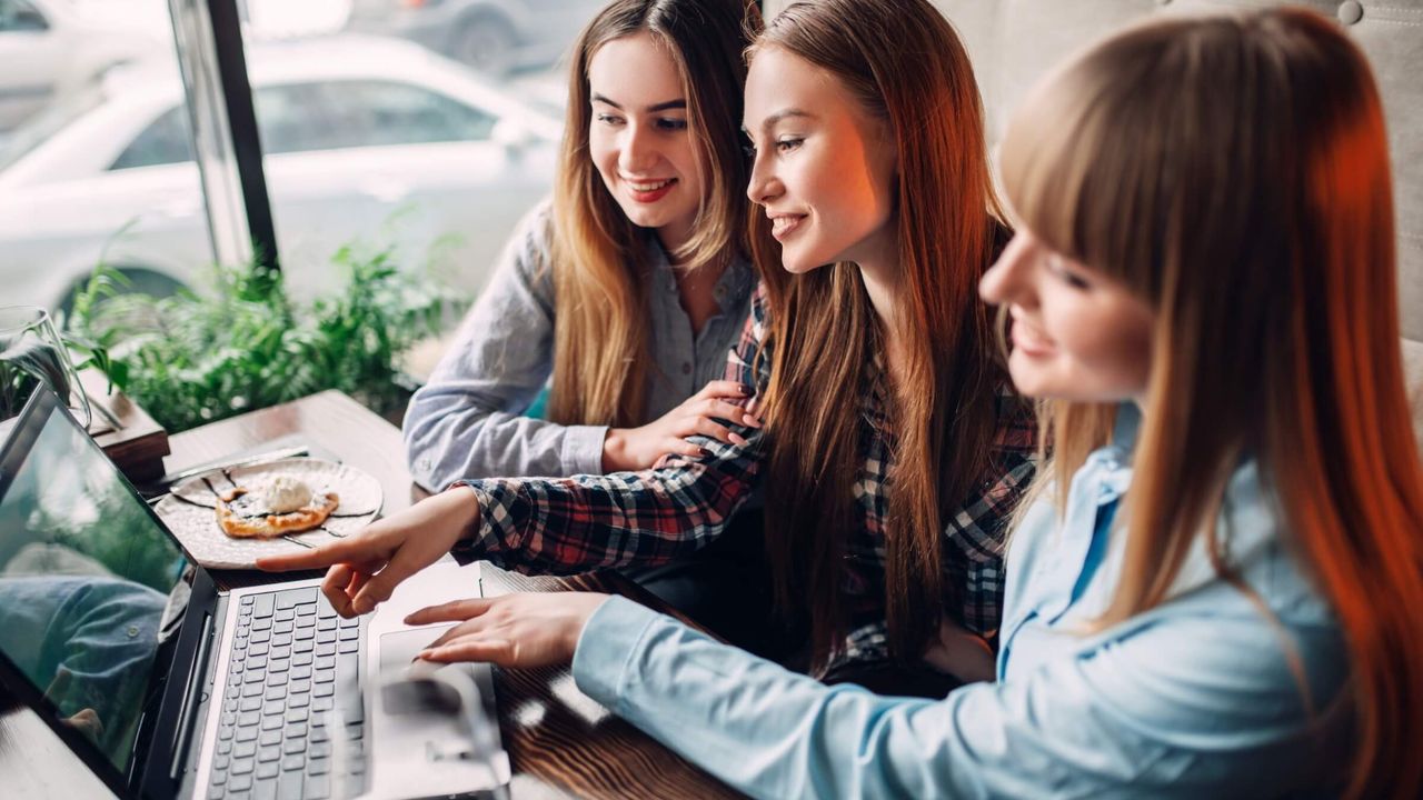 Drei glückliche junge Frauen schauen in einem Café auf einen Laptopbildschirm