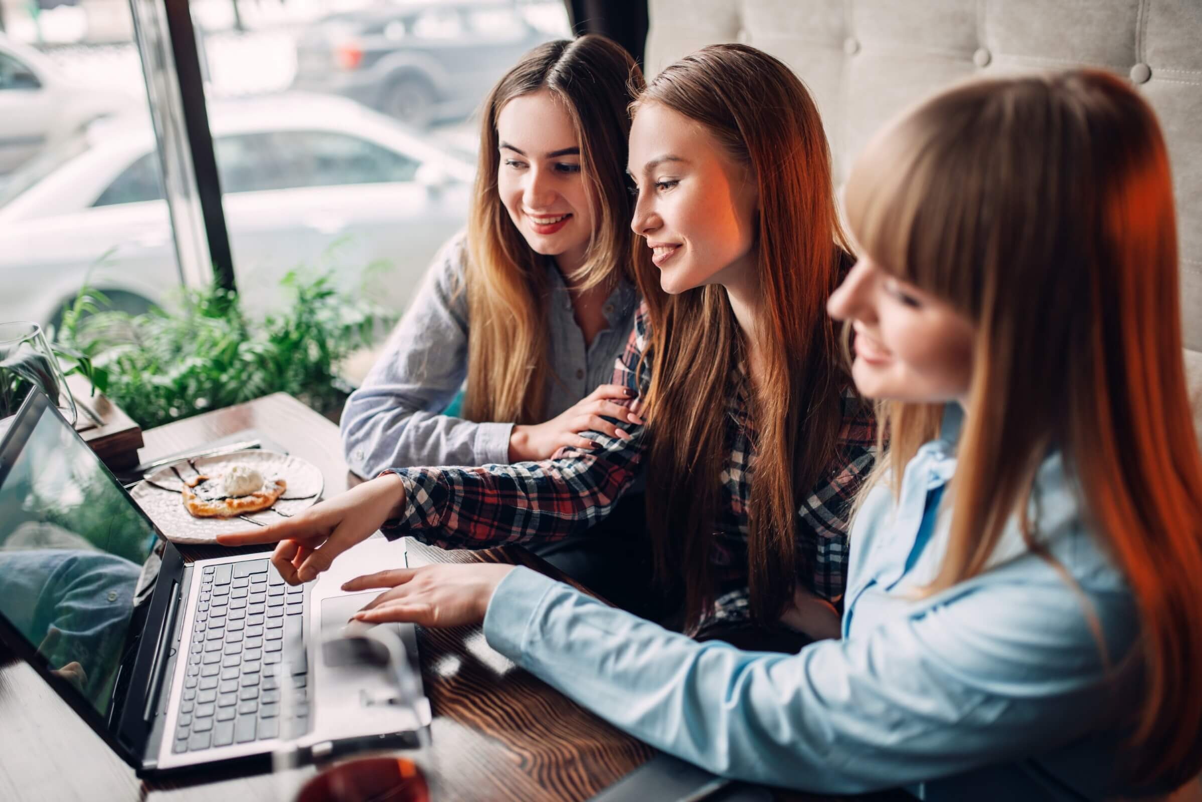 Drei glückliche junge Frauen schauen in einem Café auf einen Laptopbildschirm