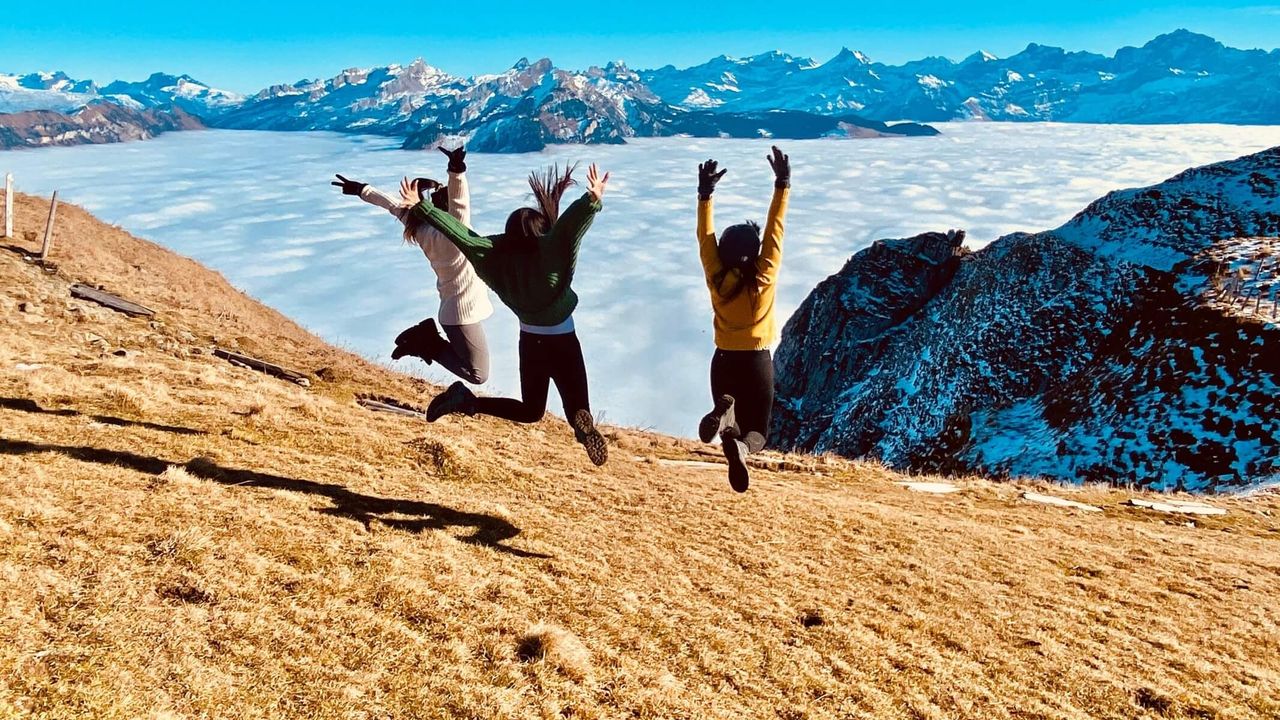 Frauen springen auf einem Hügel über Bergen und Wolken