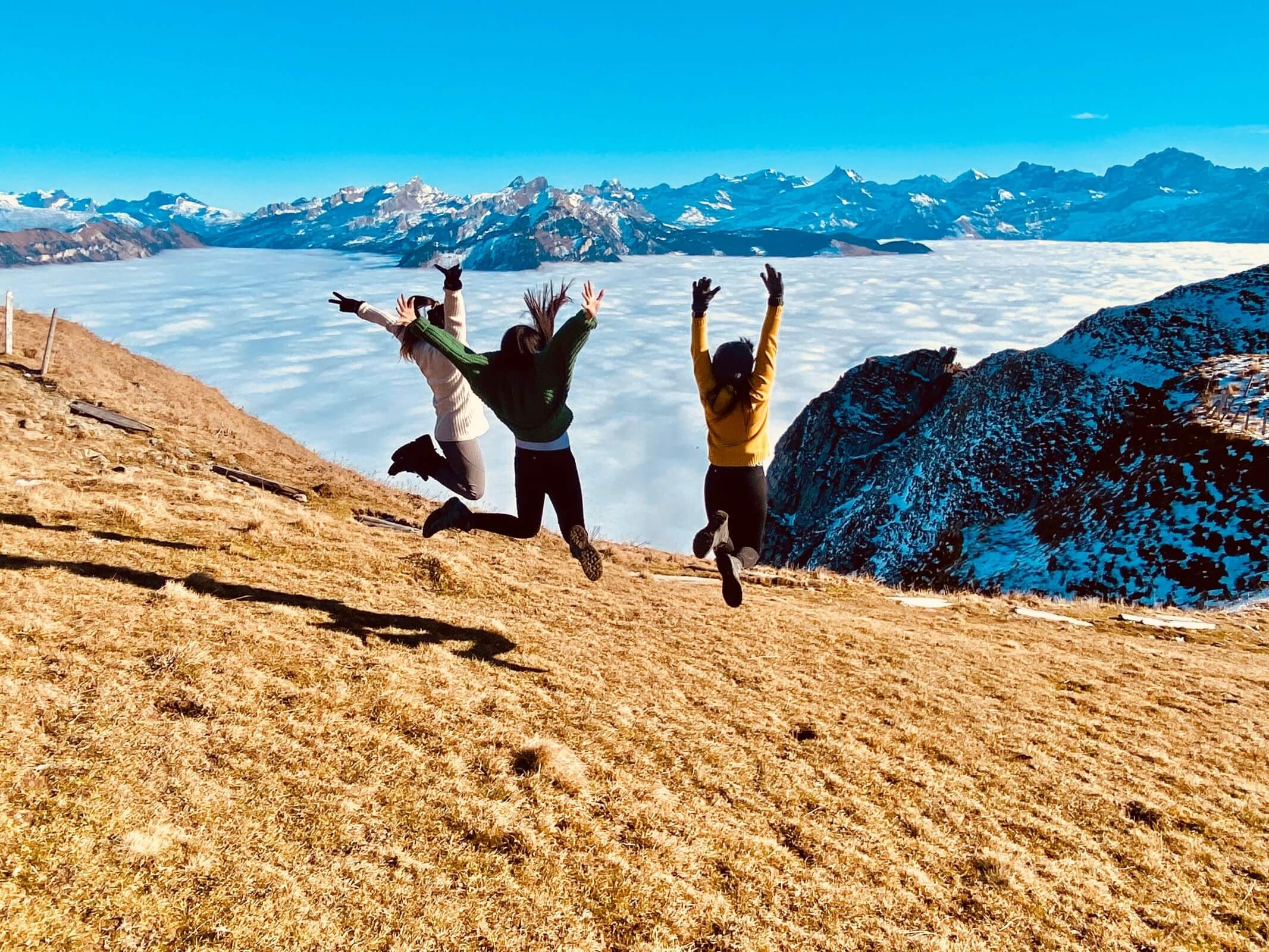 Frauen springen auf einem Hügel über Bergen und Wolken
